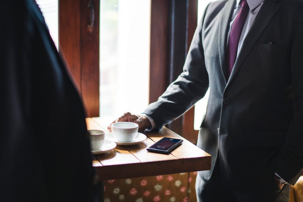 Deux hommes en costumes autour d'une table avec deux cafés et un téléphone.