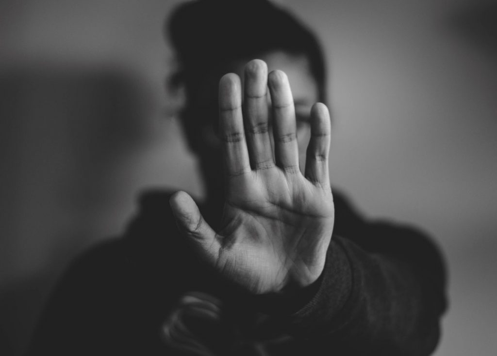 Photo noir et blanc d'une femme qui étend sa main devant son visage comme pour dire stop ou non.