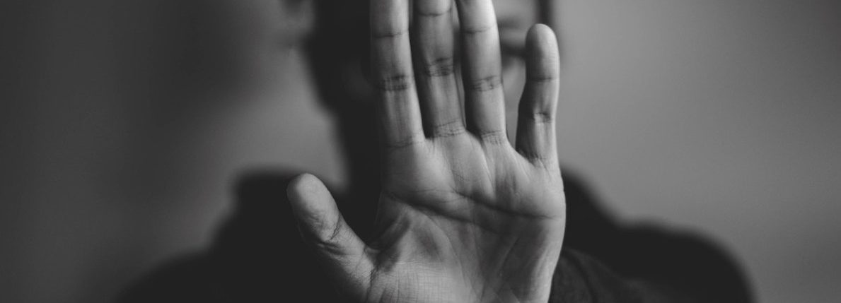 Photo noir et blanc d'une femme qui étend sa main devant son visage comme pour dire stop ou non.