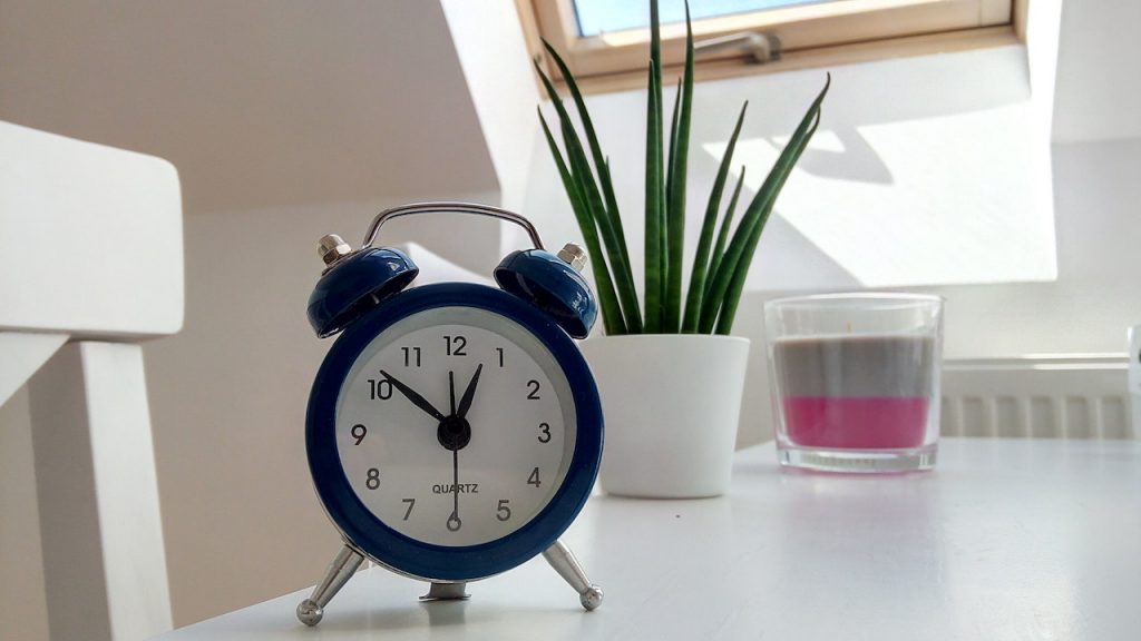 Un réveil ancien sur une table blanche à côté d'une bougie et d'une plante.