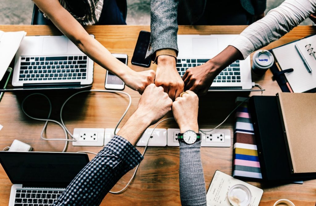 Cinq personnes rassemblent leurs poings au dessus d'une table de travail.