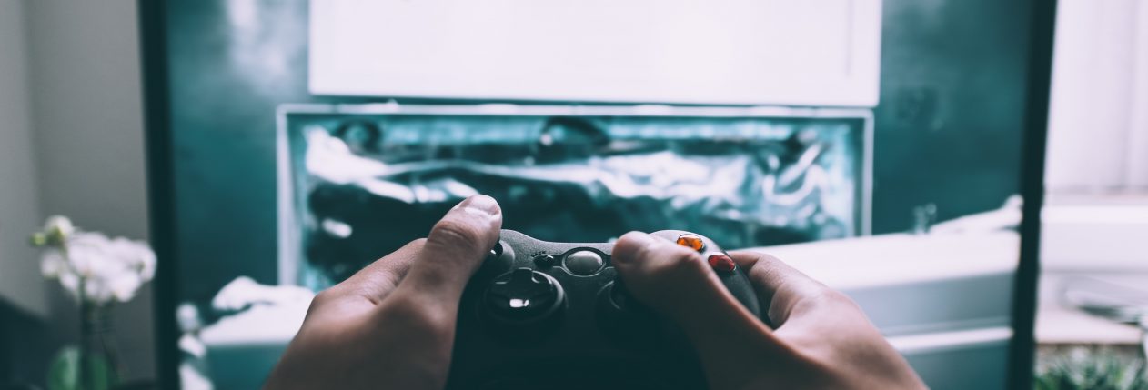 Deux mains tenant une manette de jeux vidéo devant un écran.