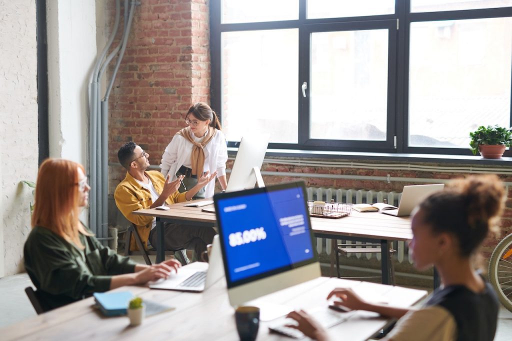 Un lieu de travail où des individus travaillent sur leurs ordinateurs. Deux d'entre eux discutent.