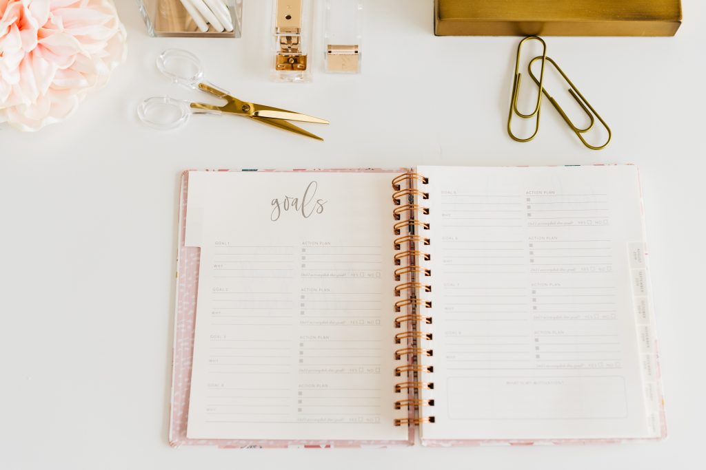 Un agenda ouvert sur une table blanche avec des fournitures dorées autour.