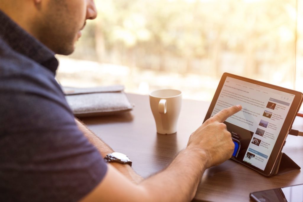 Un homme assis à une table devant une tablette avec une tasse de café.