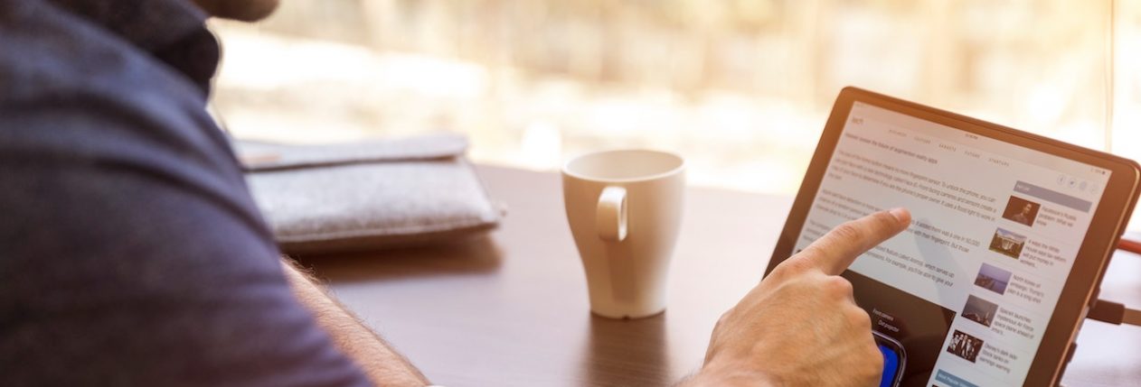 Un homme assis à une table devant une tablette avec une tasse de café.