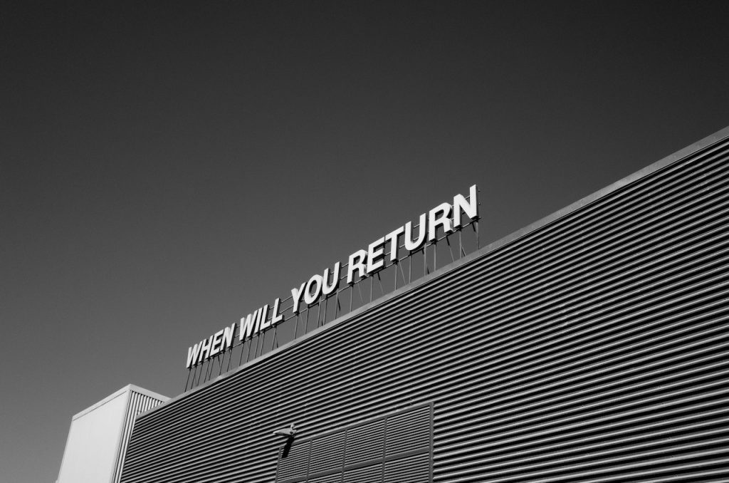 Photo en noir et blanc d'un signe en haut d'un immeuble : "When will you return"