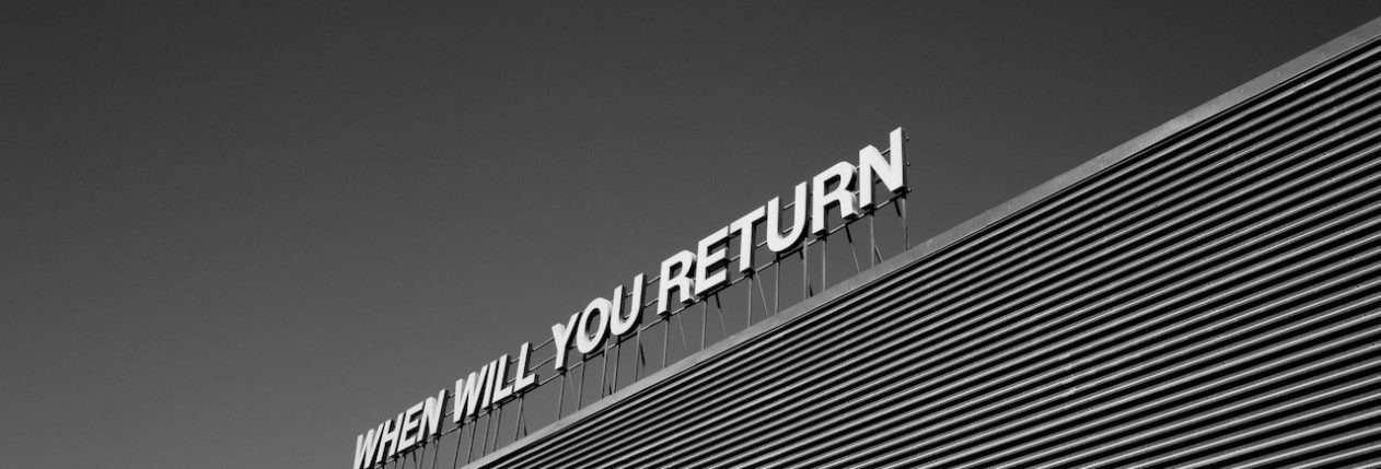 Photo en noir et blanc d'un signe en haut d'un immeuble : "When will you return"