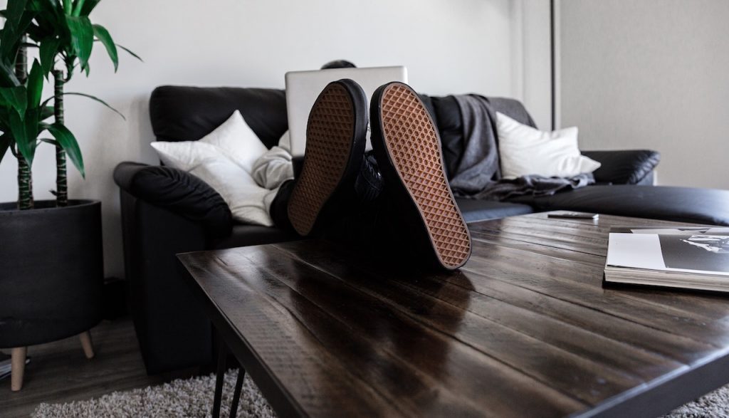 Un homme est assis sur son canapé avec un ordinateur et ses pieds sur la table basse.