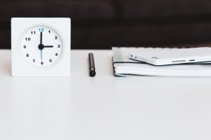 Une horloge blanche, posée sur une table à côté d'un carnet, d'un stylo et d'un téléphone.
