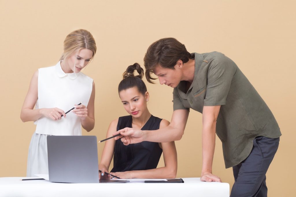 Un homme et une femme commente le travail d'une personne assise à son ordinateur.