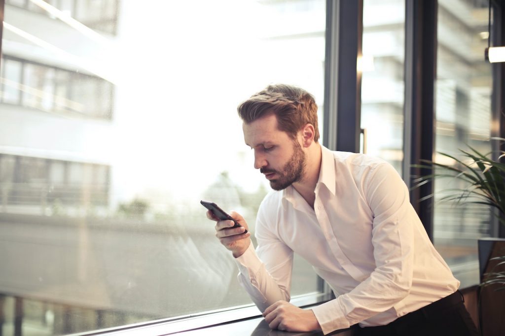 Un homme accoudé à un rebord de fenêtre regarde son téléphone.