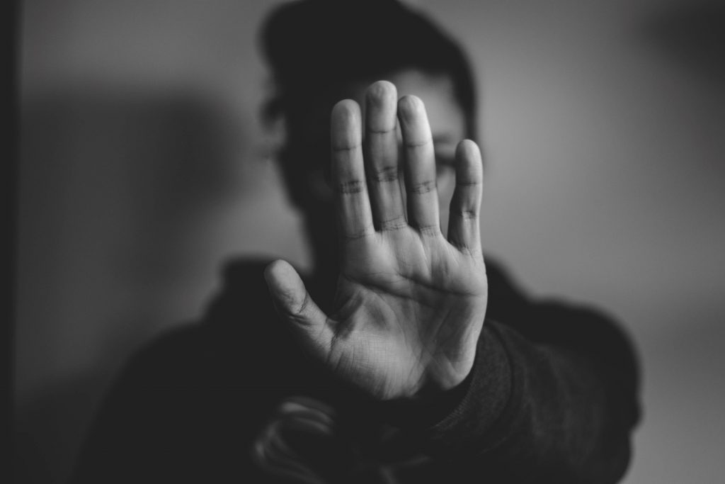 Une photo en noir et blanc où l'on voit une femme mettre sa main en avant comme pour dire "stop". Sa main cache son visage.