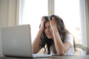 Une femme assise devant un ordinateur portable. Elle se prend la tête dans les mains et à l'air désespérée.