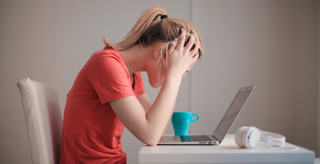 Une femme devant son ordinateur se prend la tête entre les mains. Elle a l'air stressée.