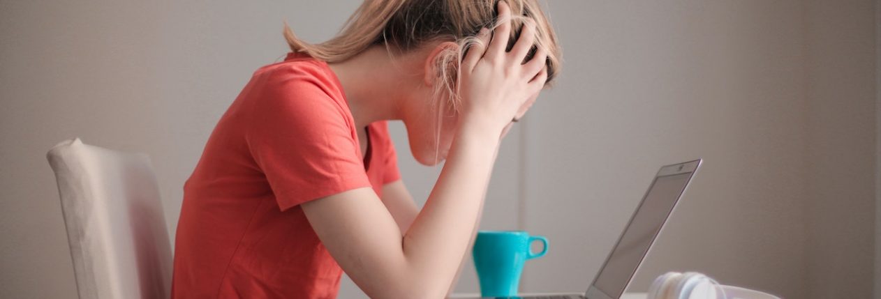 Une femme devant son ordinateur se prend la tête entre les mains. Elle a l'air stressée.