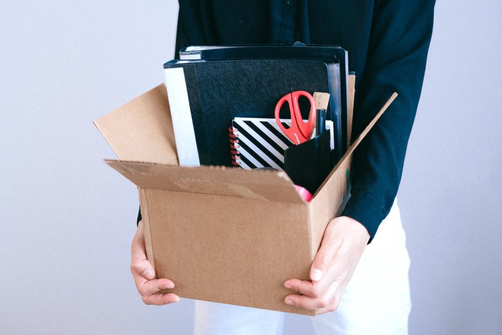 Une personne porte un carton avec ses affaires de bureau à l'intérieur.