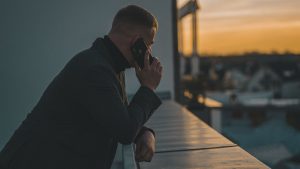 Un homme accoudé à un balcon passe un coup de téléphone en regardant à l'horizon.