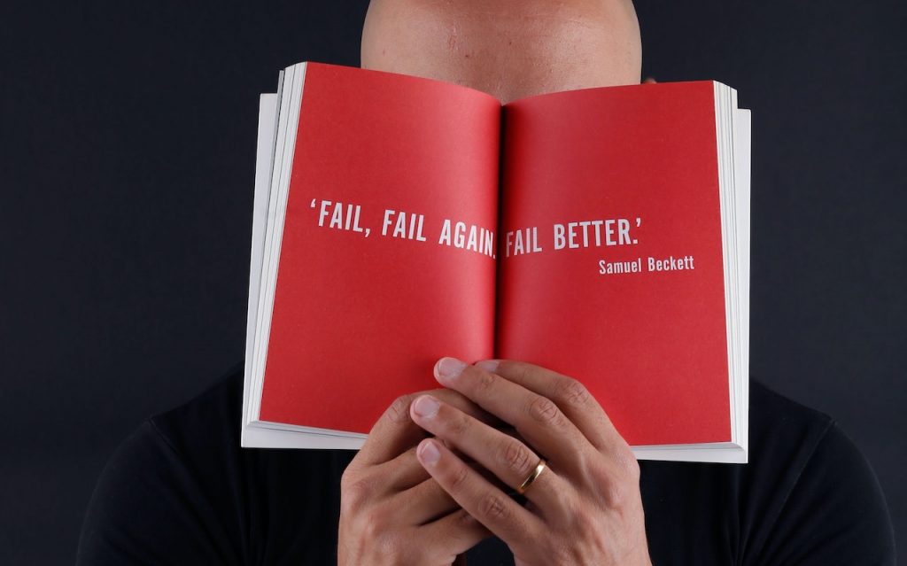 Un homme tient un livre rouge devant ses yeux avec une phrase inspirante sur l'échec.