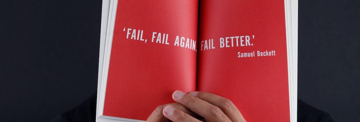 Un homme tient un livre rouge devant ses yeux avec une phrase inspirante sur l'échec.