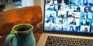 Un ordinateur ouvert sur une visio-conférence et un mug à côté.
