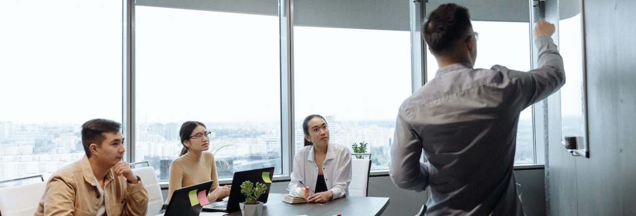 Une personne présente une idée à l'aide d'un tableau blanc au reste de son équipe, qui le regarde avec attention.