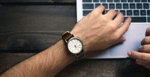 Un bras d'homme avec une montre devant un ordinateur.
