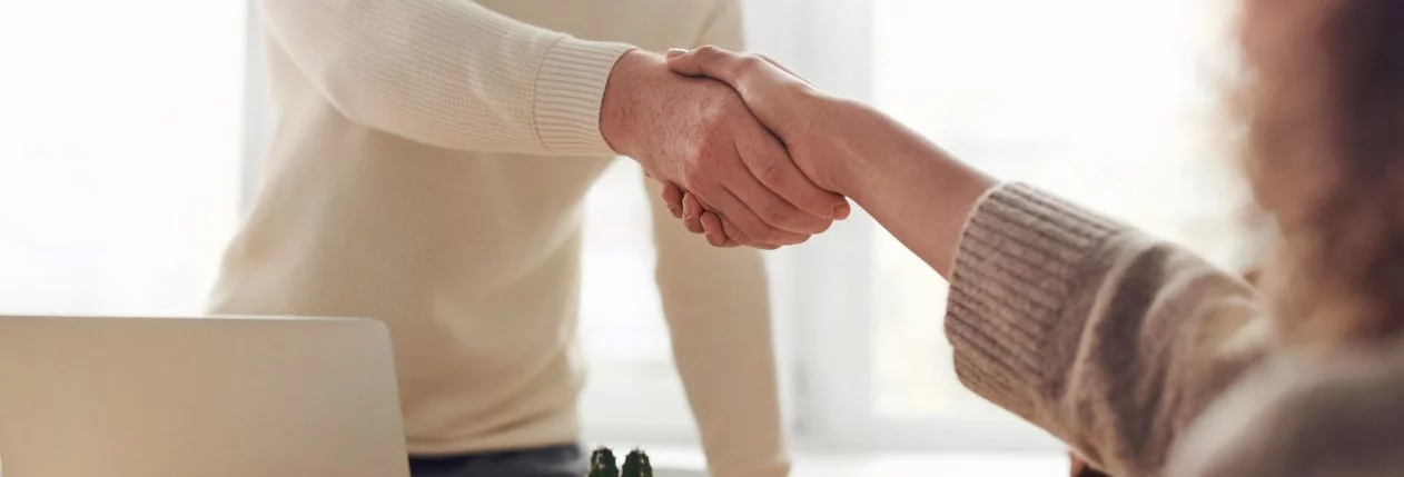Un homme debout serre la main à une femme assise derrière une bureau.