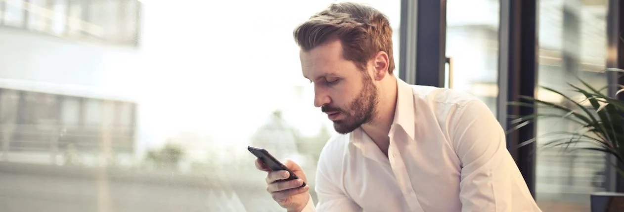 Un homme accoudé à un rebord de fenêtre regarde son téléphone.