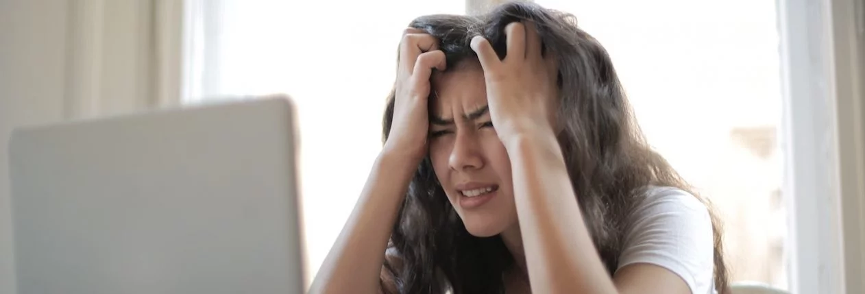 Une femme assise devant un ordinateur portable. Elle se prend la tête dans les mains et à l'air désespérée.