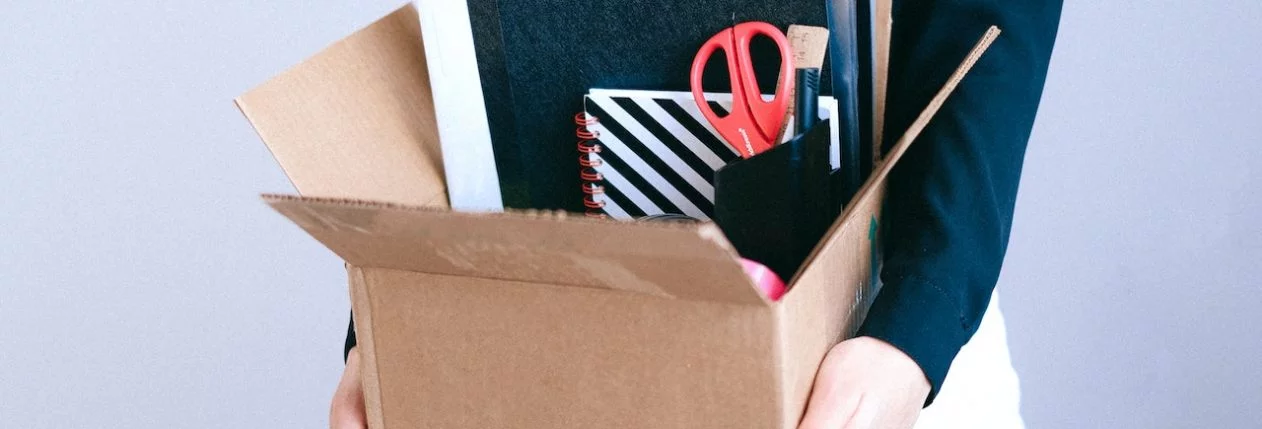 Une personne porte un carton avec ses affaires de bureau à l'intérieur.