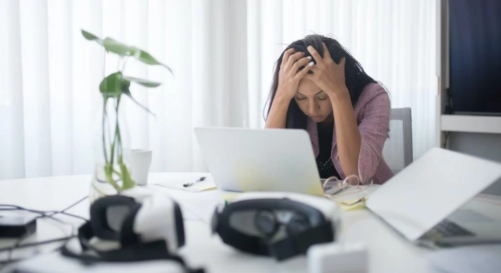 Une femme assise à son bureau, la tête dans les mains.