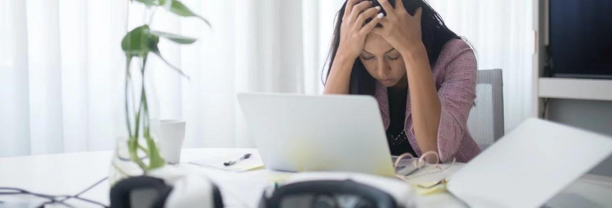 Une femme assise à son bureau, la tête dans les mains.